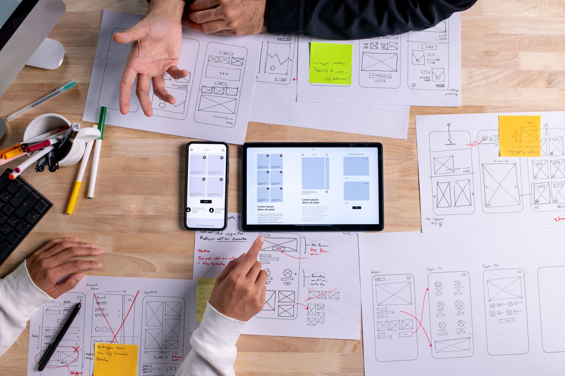UX UI designers discussing and brainstorming on wireframes for a website and mobile app prototype, surrounded by sketches of user flow and design tools, in the concept of website and mobile application design concept.